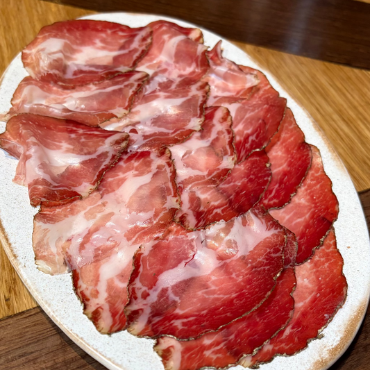Sliced cured meat on a white plate on a wooden surface