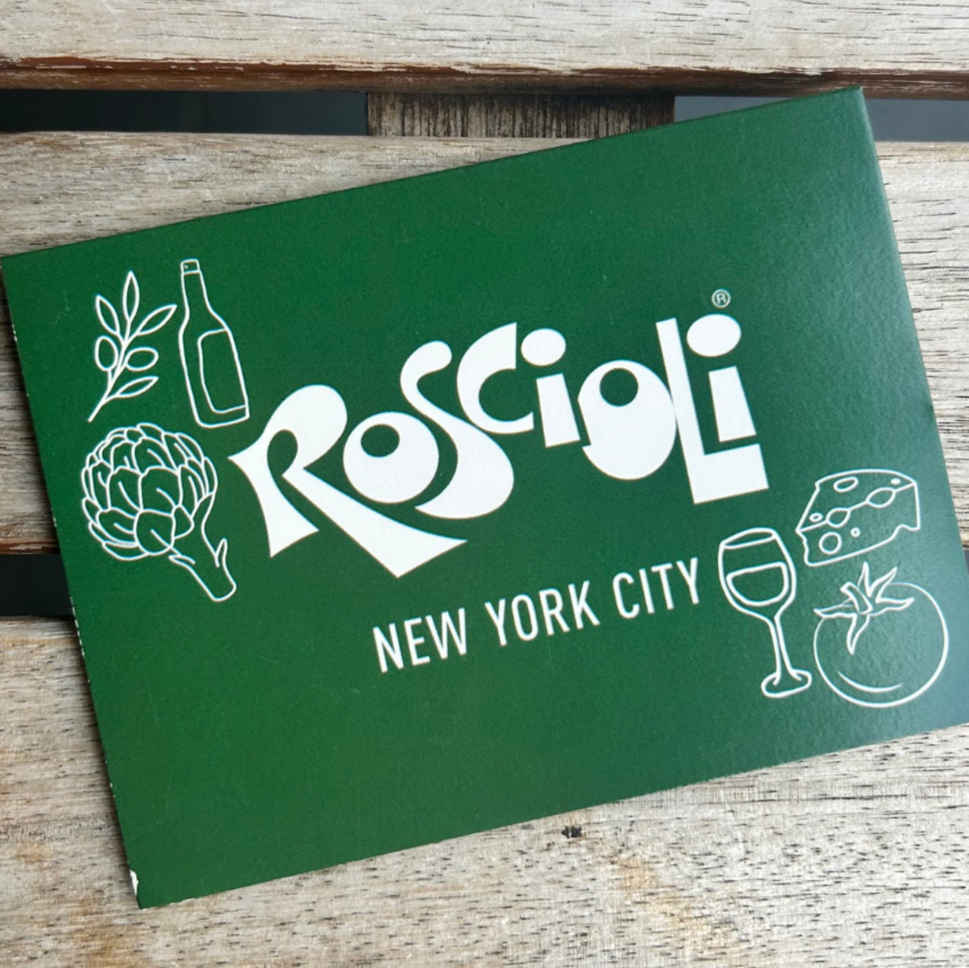 Green card with 'Roscioli New York City' logo and illustrations on a wooden surface