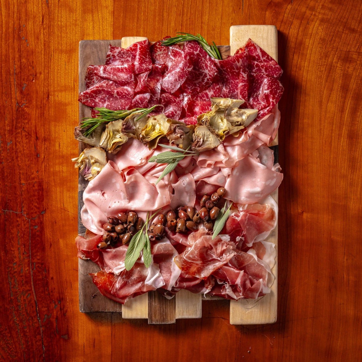 Wooden cutting board with various cured meats and olives on a wooden surface